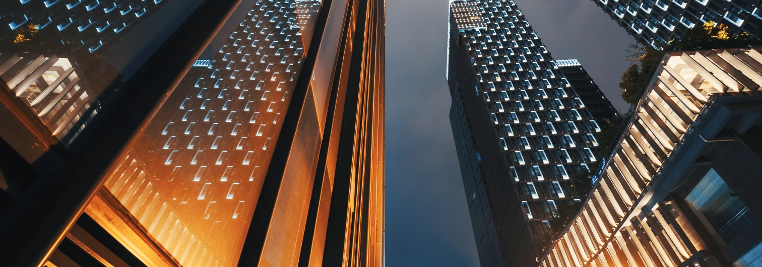 Low-angle view of illuminated modern skyscrapers glowing gold and blue against evening sky.